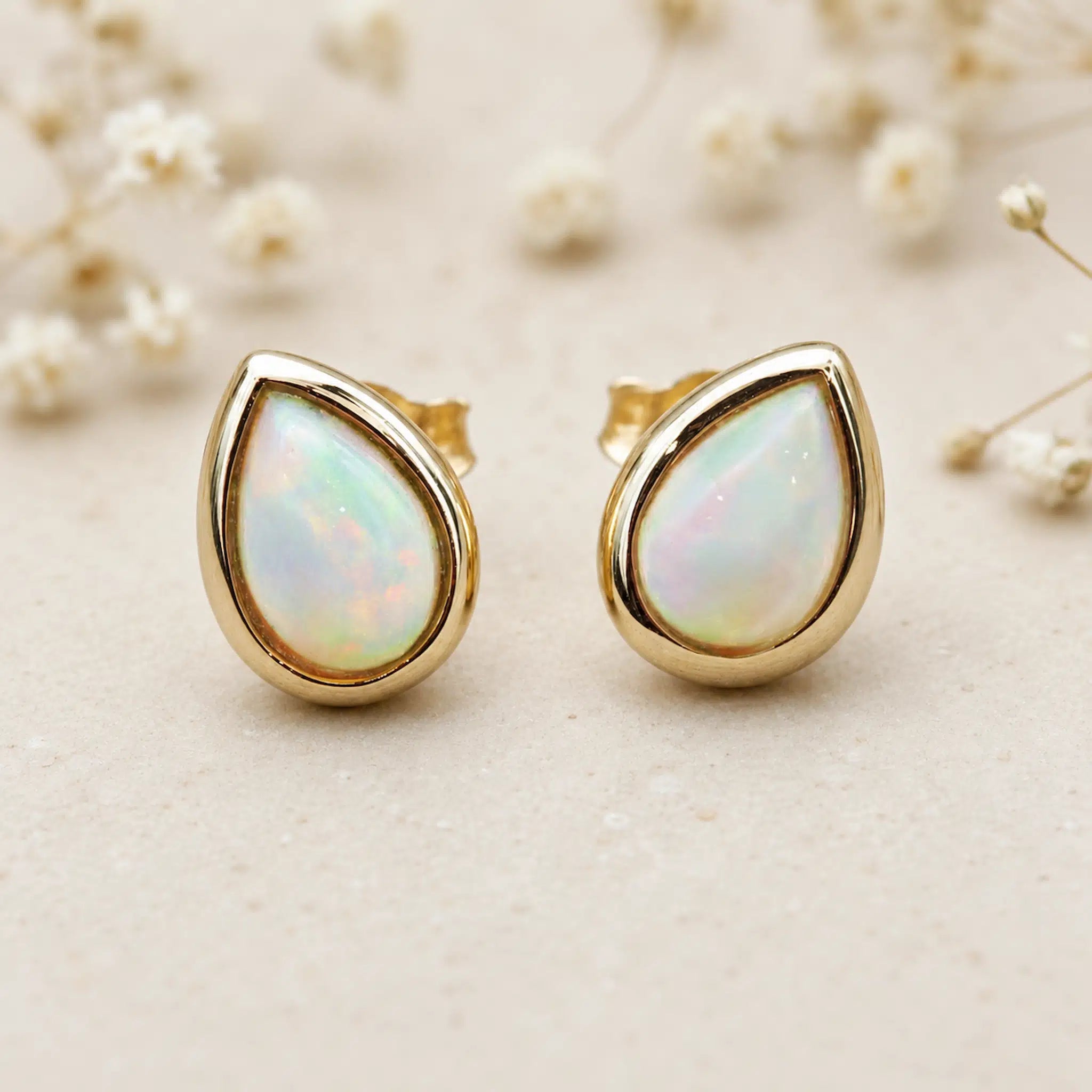 Pair of Gold October Birthstone Earrings in pear-shaped cabochon stud style with natural opal gemstones on a light surface.
