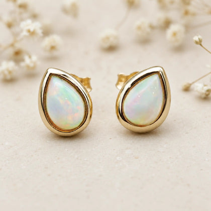 Pair of Gold October Birthstone Earrings in pear-shaped cabochon stud style with natural opal gemstones on a light surface.