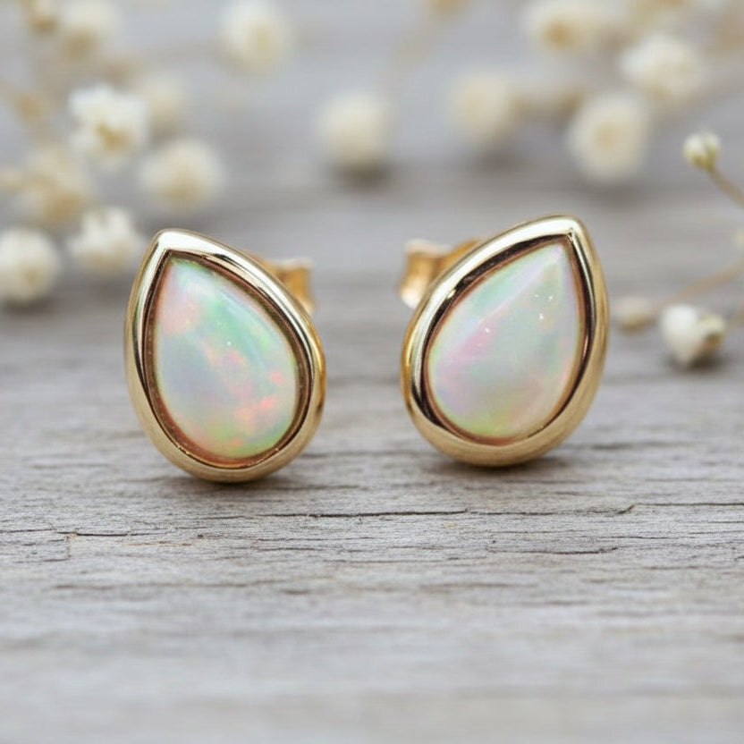 Gold earrings with opal stones on a wooden surface with blurred flowers in the background