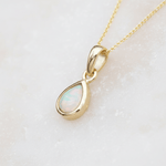 Gold pendant with a teardrop-shaped opal stone on a light background