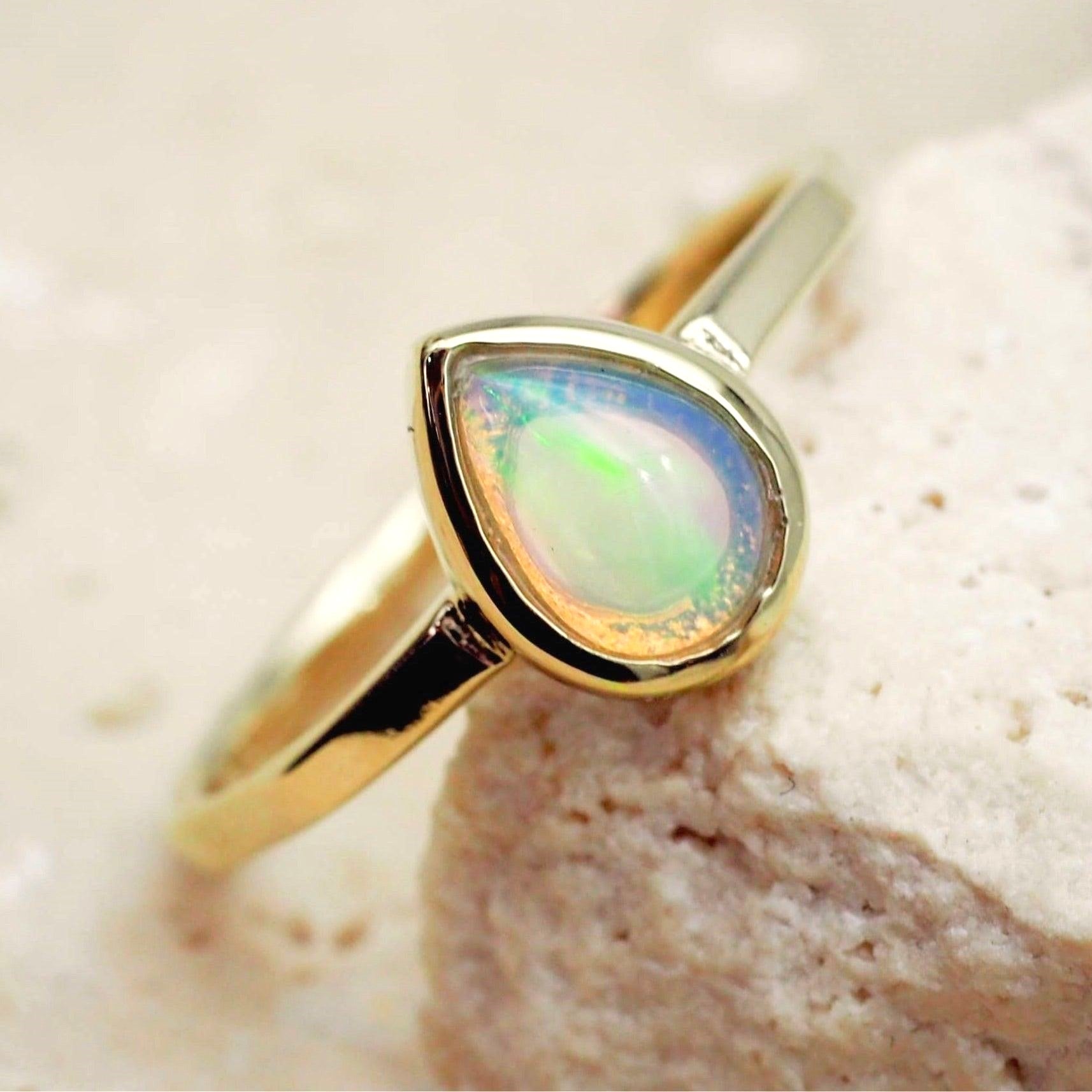 Gold ring with a teardrop-shaped opal stone on a beige background