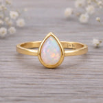 gold ring with tear drop shaped natural opal on a wooden surface
