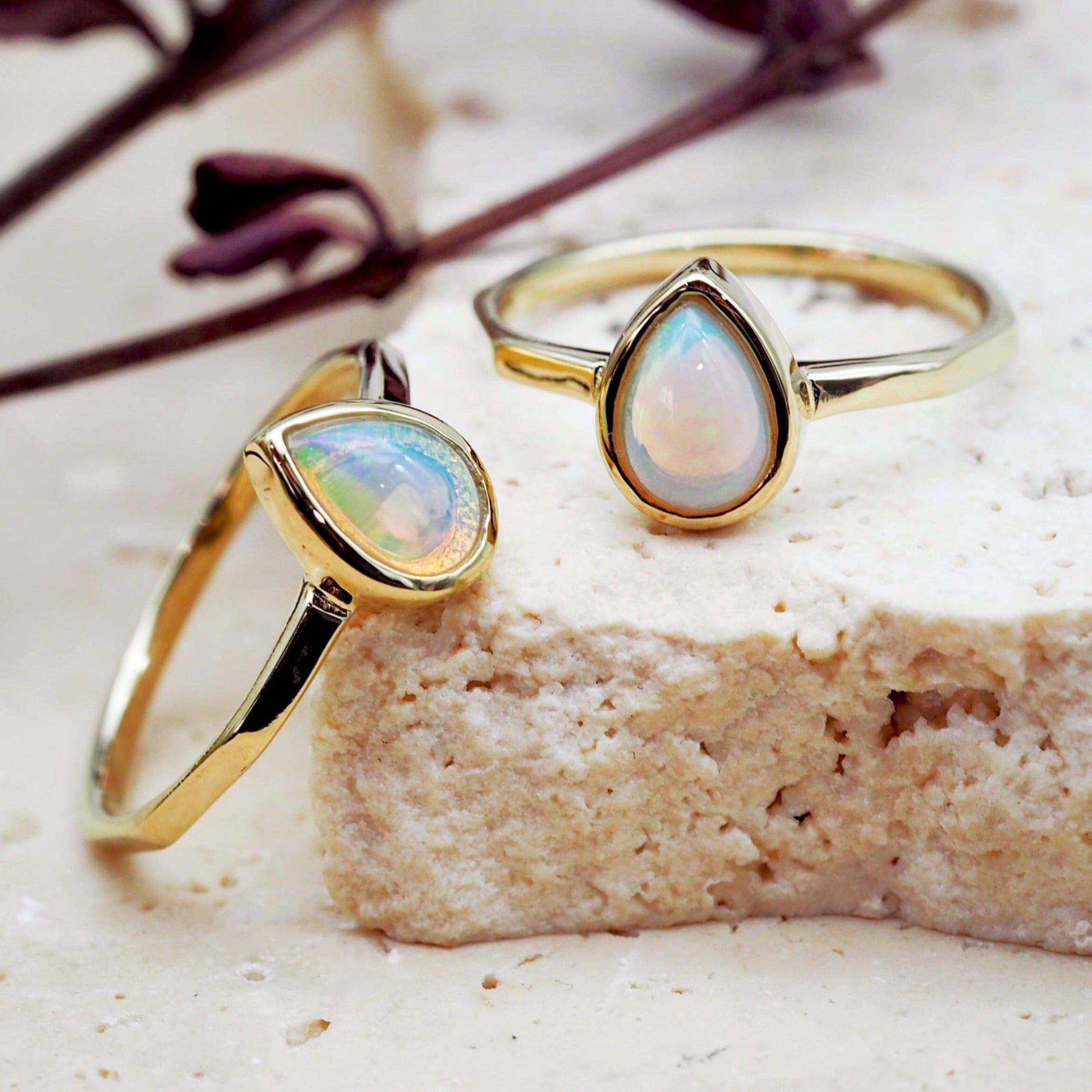 Two gold-finish October birthstone opal rings with pear-shaped natural opals in polished bezel settings.