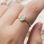 Gold October birthstone ring with opal stone on a person's finger against a neutral background