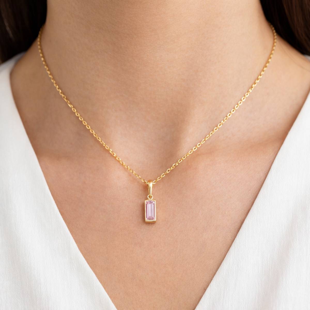 Gold necklace with a pink gemstone pendant on a person wearing a white top.