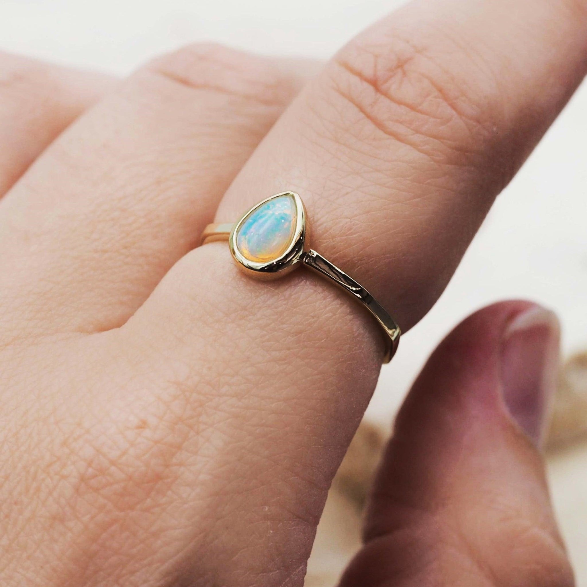 Gold October birthstone ring with opal stone on a person's finger against a neutral background
