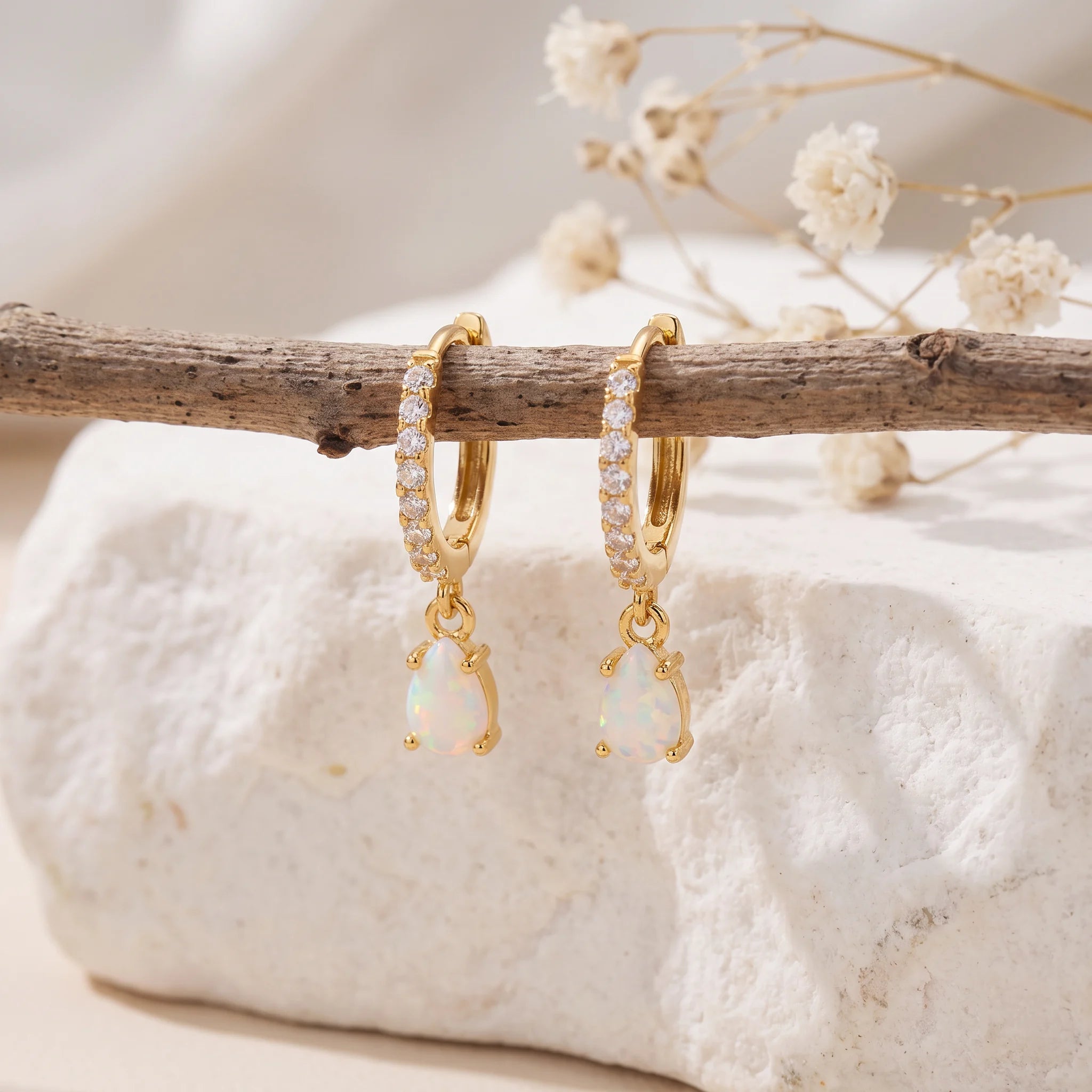 Gold opal teardrop huggie earrings hanging from a rustic branch over white stone