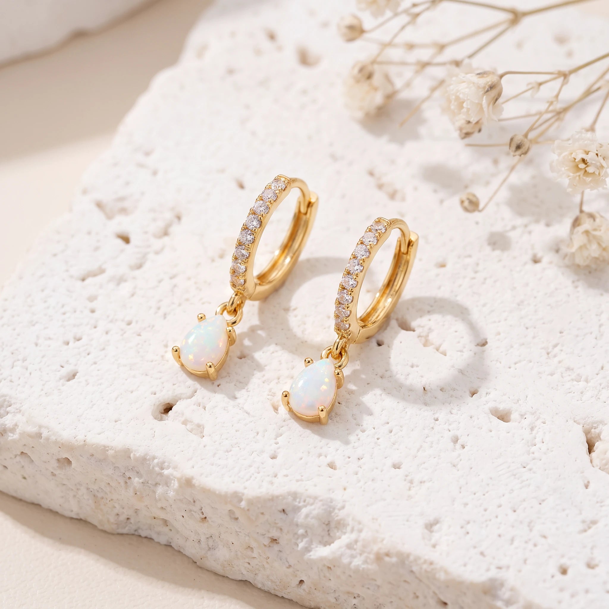 Gold opal teardrop huggie earrings flat lay on white textured stone with dried baby's breath