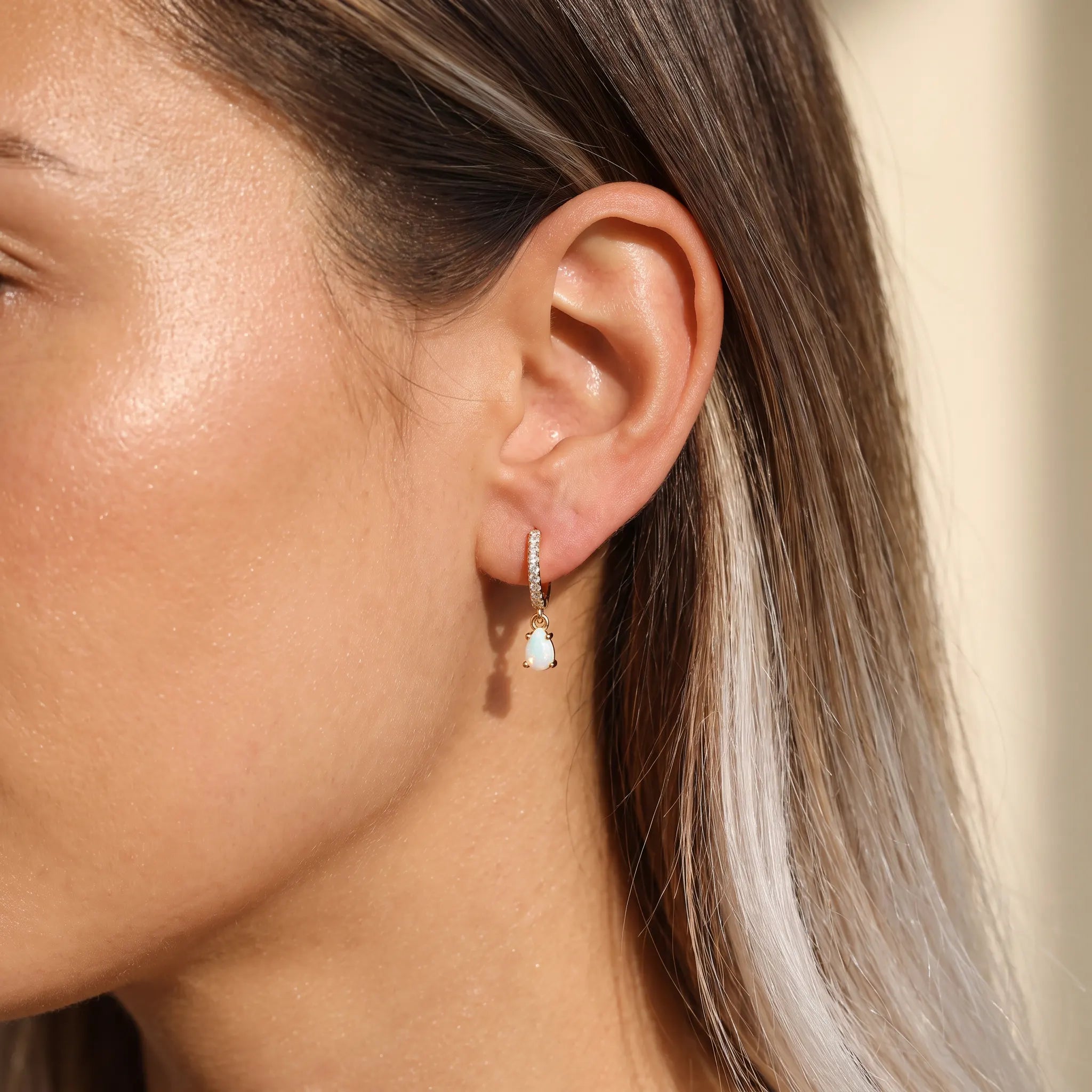 Gold opal teardrop huggie earrings worn on the ear, dainty pavé hoop with opal drop