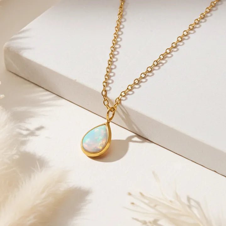 Gold necklace with a teardrop-shaped opal pendant on a white surface