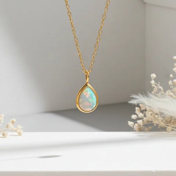 Gold necklace with a teardrop-shaped opal pendant on a neutral background