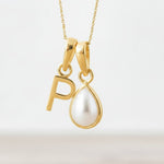 Gold necklace with a 'P' pendant and teardrop-shaped pearl on a light background