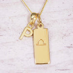 Gold initial and Libra zodiac necklace with a letter P charm and engraved bar pendant on whitewashed wood