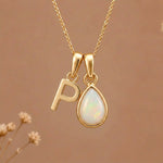 Gold Initial P Pendant and October birthstone Natural Opal Necklace against a warm background