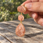 Gold peach sandstone drop earring held at a slight angle, showing the gold setting and creamy markings in the peach stones.