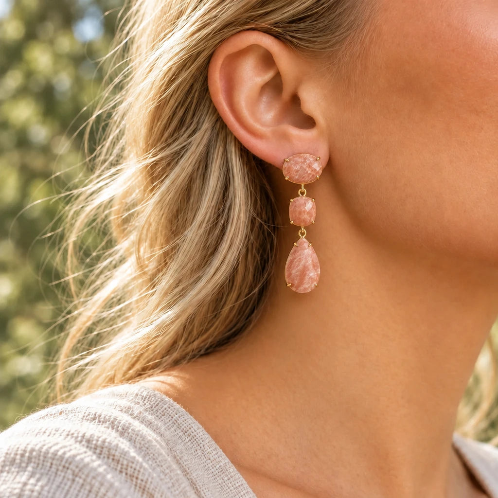Gold peach sandstone drop earring worn in soft daylight, showing peach stones with creamy markings and gold claw settings.