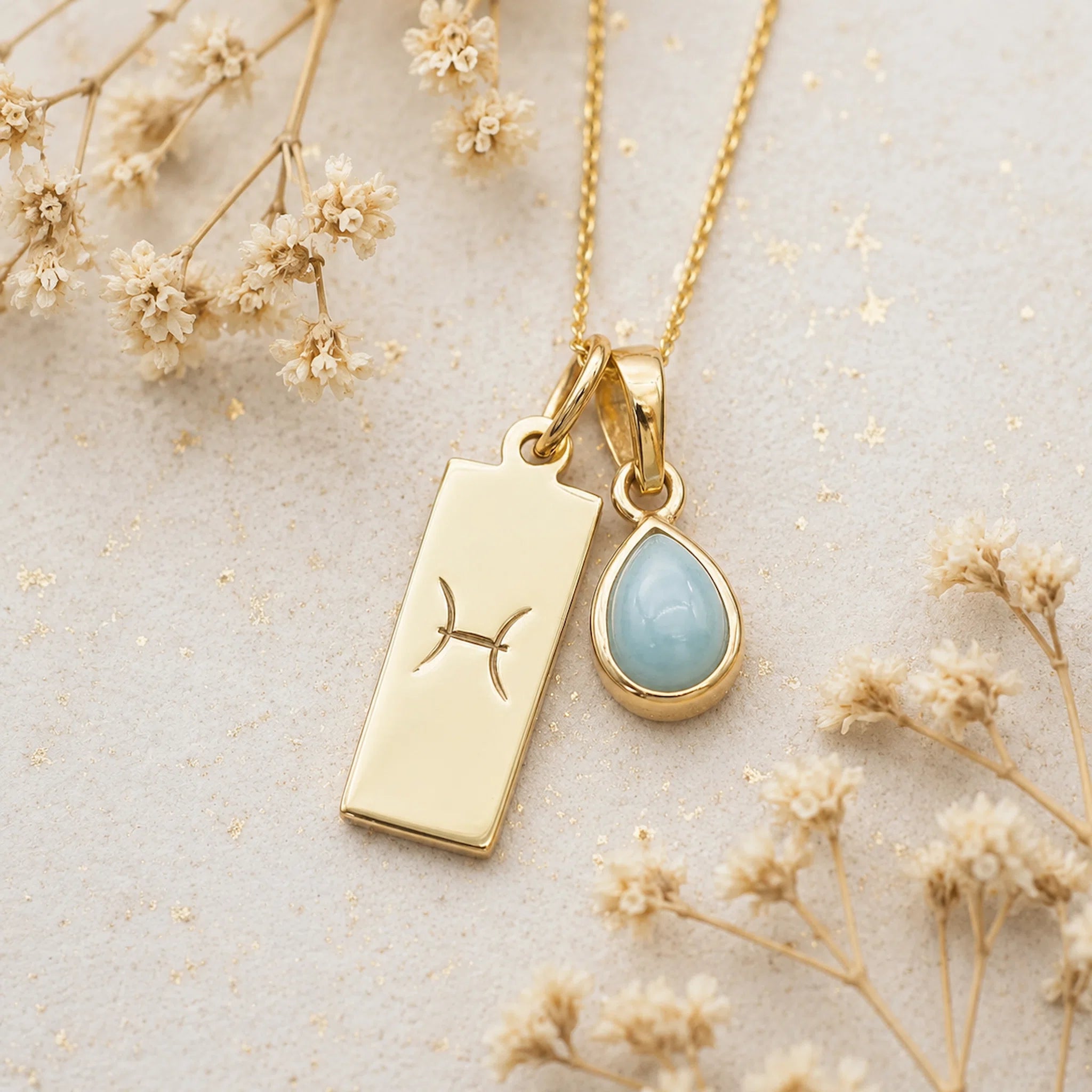 Gold Necklace with teardrop March Birthstone Natural Aquamarine pendant and a rectangle pendant wth Pisces line glyph on a light background.