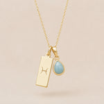 Gold Necklace with teardrop March Birthstone Natural Aquamarine pendant and a rectangle pendant wth Pisces line glyph hanging on a light background.