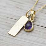 Gold necklace with a purple teardrop pendant on a wooden surface