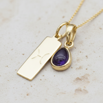 Gold pisces zodiac necklace with a purple amethyst teardrop pendant on a stone surface