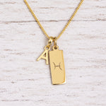 Gold Pisces initial necklace with a letter A charm and engraved zodiac bar on white wood, close-up