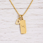 Gold Pisces initial necklace with a letter D charm and engraved zodiac bar on white wood, close-up