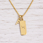 Gold Pisces initial necklace with a letter F charm and engraved zodiac bar on white wood, close-up