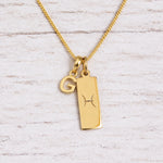 Gold Pisces initial necklace with a letter G charm and engraved zodiac bar on white wood, close-up