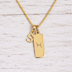 Gold Pisces initial necklace with a letter S charm and engraved zodiac bar on white wood, close-up