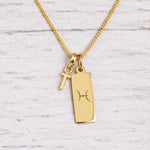 Gold Pisces initial necklace with a letter T charm and engraved zodiac bar on white wood, close-up
