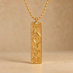 Gold Pisces zodiac necklace, embossed bar pendant with sign symbol on a faceted ball chain, warm beige background