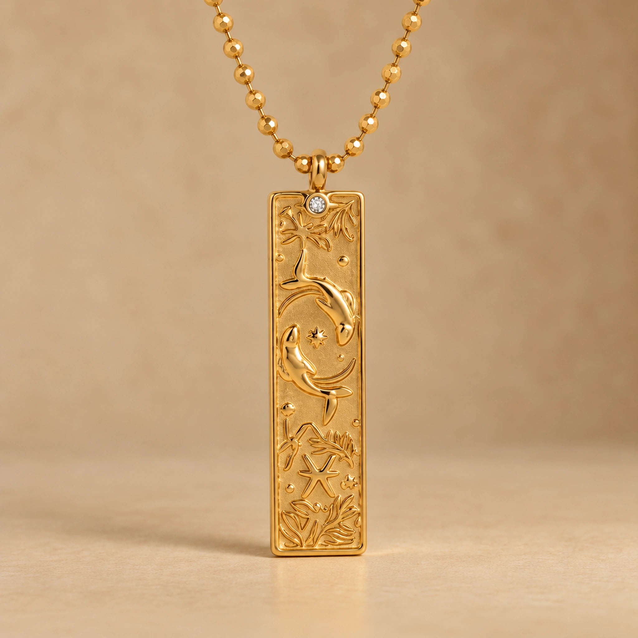 Gold Pisces zodiac necklace, embossed bar pendant with sign symbol on a faceted ball chain, warm beige background