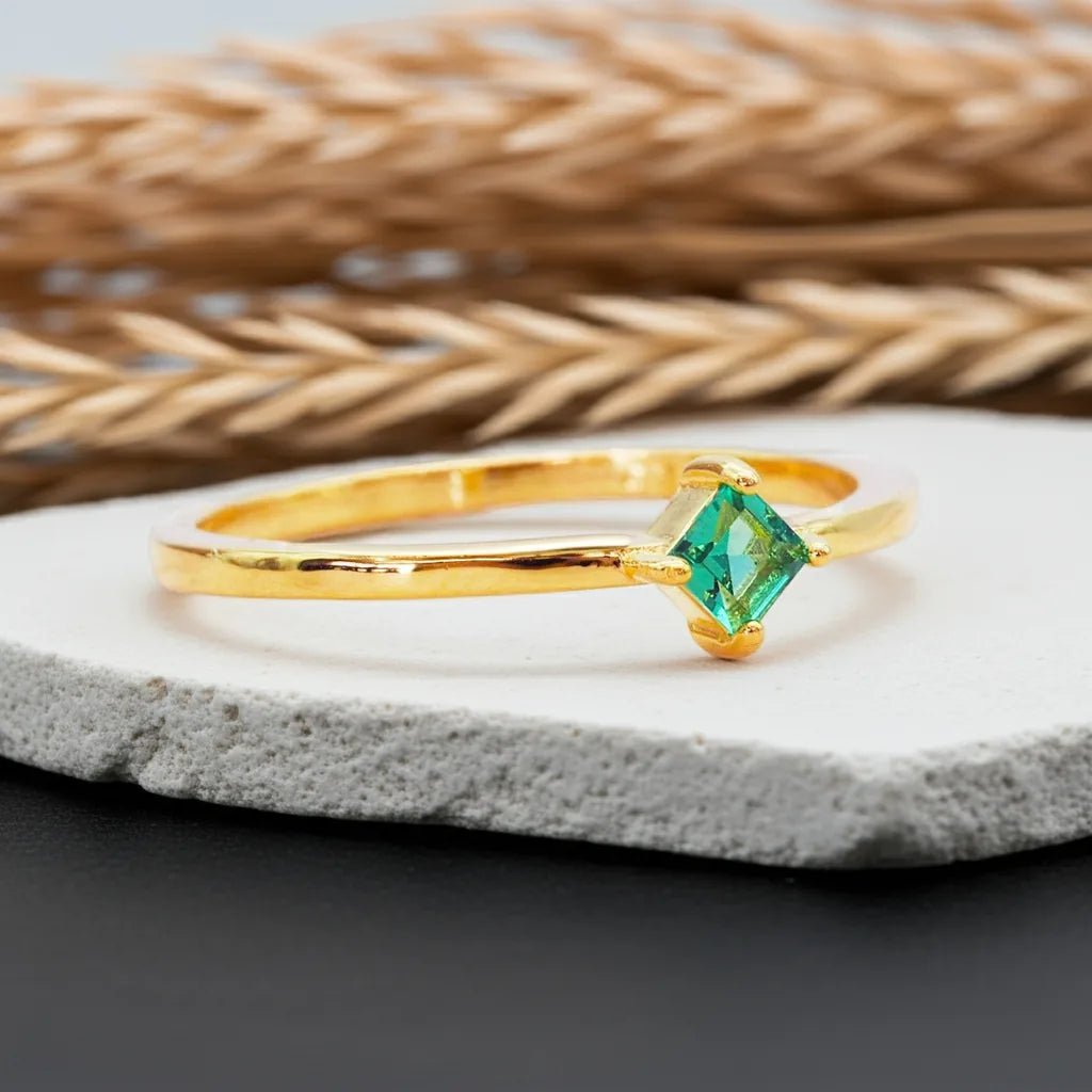 Gold ring with a green gemstone on a stone surface with woven material in the background