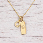 Gold Initial Q Pendant and Cancer Zodiac Pendant Necklace on a fine gold chain against a light wooden background
