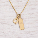 gold Q initial and aquarius zodiac necklace on fine gold chain against a light wooden background