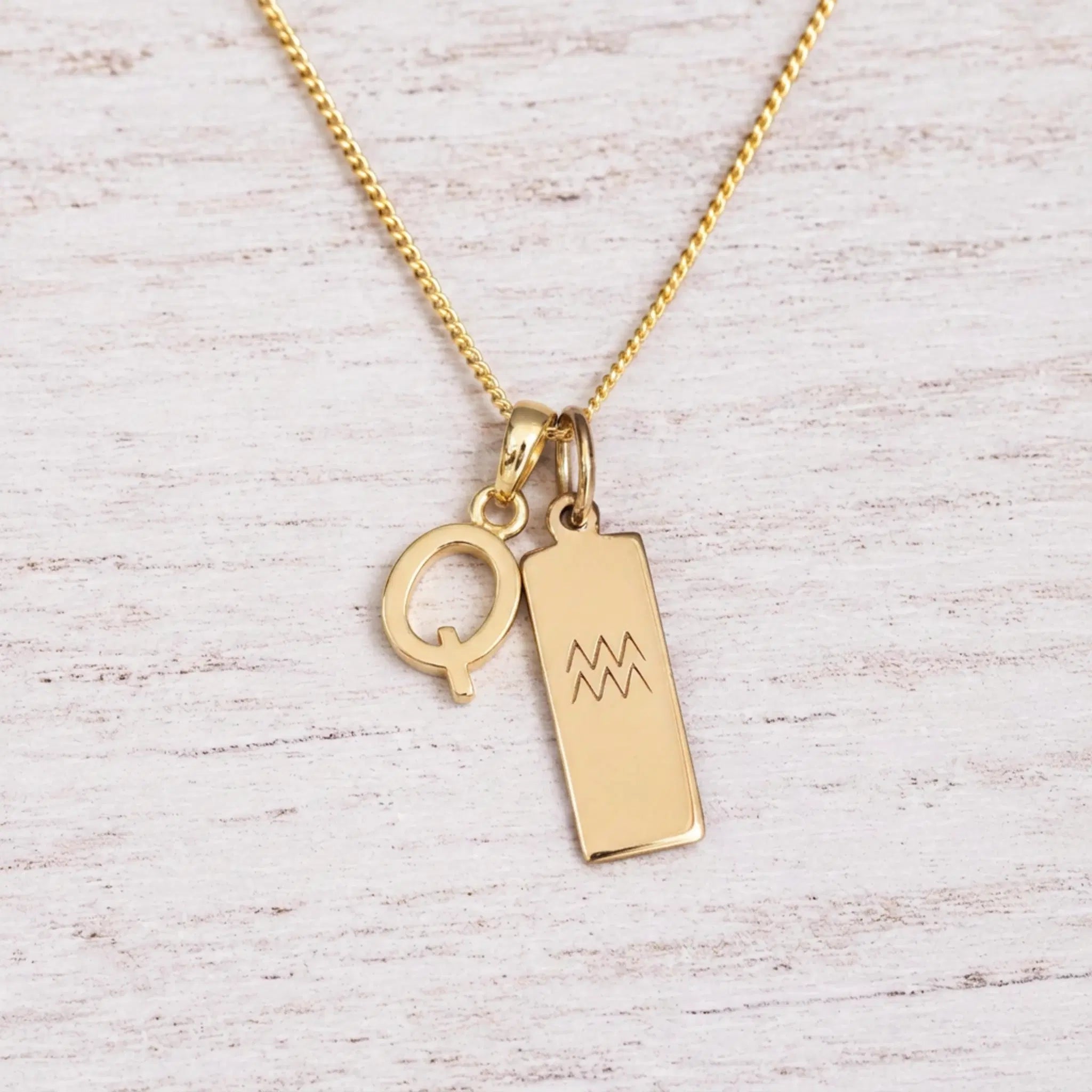 gold Q initial and aquarius zodiac necklace on fine gold chain against a light wooden background