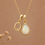 Gold Initial Q Pendant and October birthstone Natural Opal Necklace against a warm background