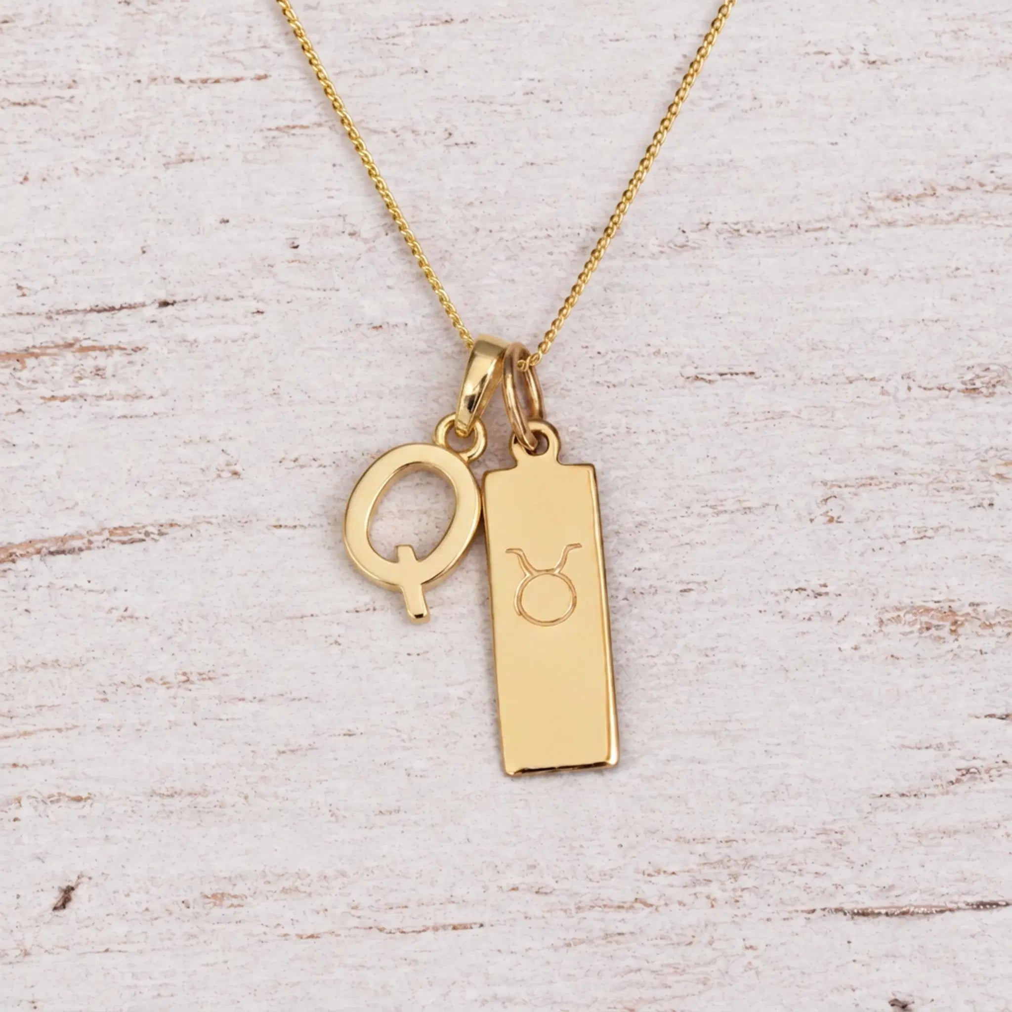 Gold Q Initial and Taurus Necklace on a fine gold chain against a light wooden background
