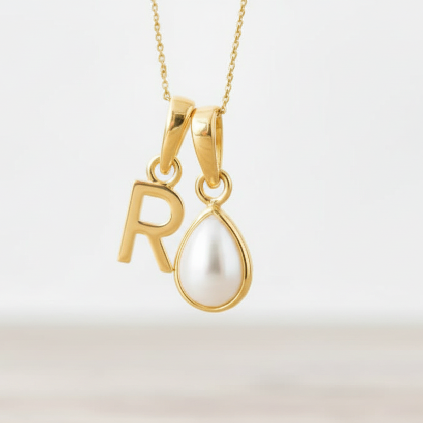 Gold necklace with 'R' pendant and teardrop-shaped pearl on a light background