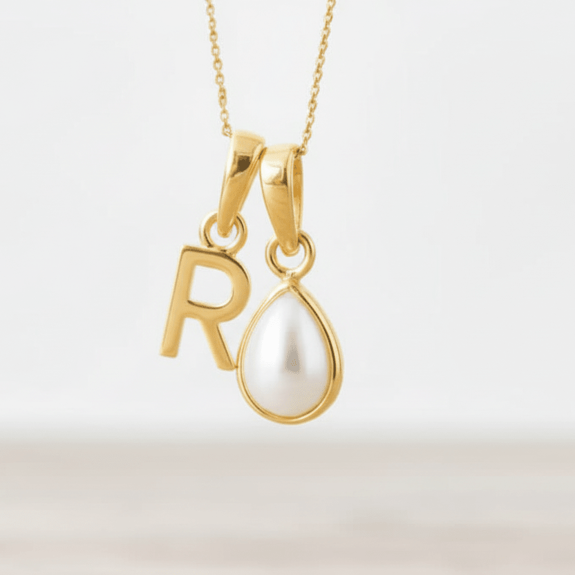 Gold necklace with 'R' pendant and teardrop-shaped pearl on a light background