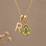Gold Initial R Pendant and August birthstone Natural Peridot Necklace against a warm background
