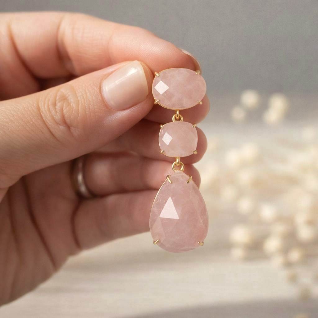 Rose quartz teardrop earrings held by a hand with a blurred background