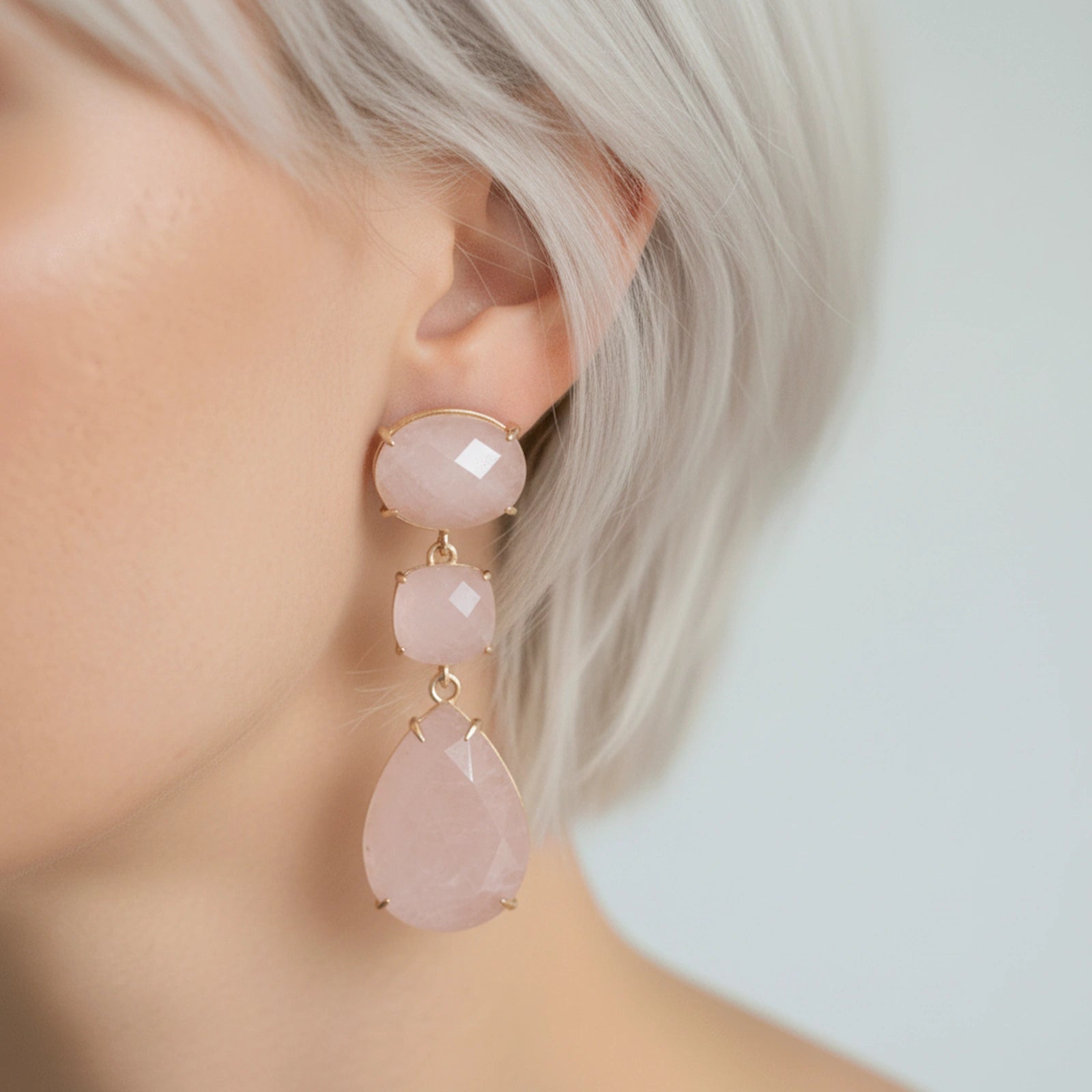 Close-up of an ear wearing a pair of pink teardrop earrings with gold accents.