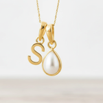 Gold necklace with a 'S' pendant and a teardrop-shaped pearl on a light background