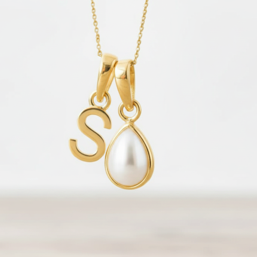 Gold necklace with a 'S' pendant and a teardrop-shaped pearl on a light background