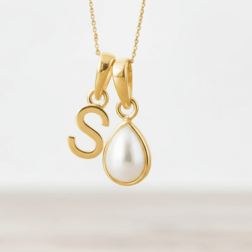 Gold necklace with a 'S' pendant and a teardrop-shaped pearl on a light background