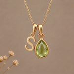 Gold Initial S Pendant and August birthstone Natural Peridot Necklace against a warm background