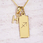 Gold Sagittarius initial necklace with a letter H charm and engraved zodiac bar on white wood, close-up
