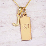 Gold Sagittarius initial necklace with a letter J charm and engraved zodiac bar on white wood, close-up
