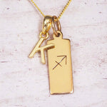 Gold Sagittarius initial necklace with a letter K charm and engraved zodiac bar on white wood, close-up